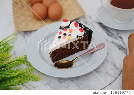 A delicious slice of chocolate cake with cherry topping on a white plate. 126119776