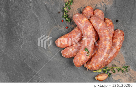 Raw sausages or bratwurst with spices for grill or barbeque on a black stone table, top view 126120290