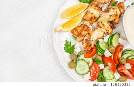 chicken kebab or souvlaki. Mediterranenan healthy lunch greek salad, tzatziki yogurt sauce chicken skewers on white background, top view, copy space 126120352