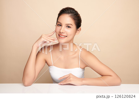 A beautiful young Asian woman with clean, fresh skin against a beige background. Skincare, facial treatment, cosmetology, beauty, and spa. An elegant portrait of an Asian woman. 126120824