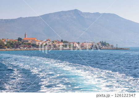 Orebic town at coast of the Peljesac peninsula in Croatia, Europe. Coastal European town with orange rooftops and a backdrop of a mountain viewed from the water. Calm ocean water. 126122347