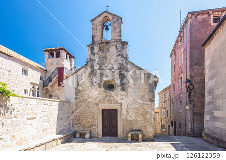 Korcula town in island of Korcula in Adriatic sea in Croatia, Europe. Historic church with aged stone facade and bell tower, set against a bright blue sky in a charming European town. Korcula town in island of Korcula in Adriatic sea in Croatia, Europe. Historic church with aged stone facade and bell tower, set against a bright blue sky in a charming European town. 126122359