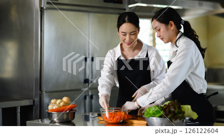 Two female culinary students preparing vegetables during a cooking class in a professional kitchen Two female culinary students preparing vegetables during a cooking class in a professional kitchen 126122604