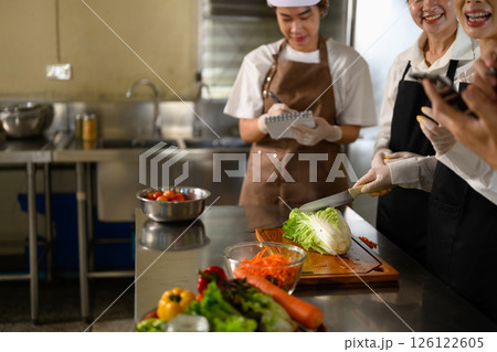 Cooking students attentively watching their teacher demonstrate food preparation techniques 126122605