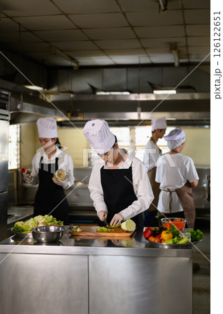 Chef apprentice working on vegetable preparation in a busy kitchen. 126122651