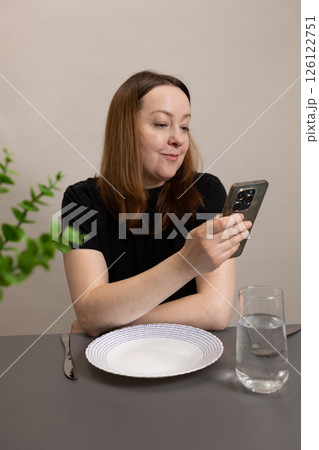 A woman is engaging attentively with her smartphone while sitting at the dining table A woman is engaging attentively with her smartphone while sitting at the dining table 126122751