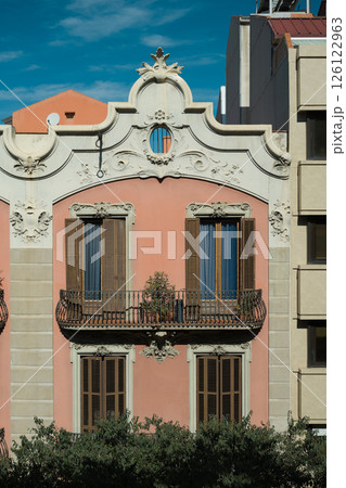 Facade of elegant pink historic building in Barcelona with ornate white decorations and wooden shutters Facade of elegant pink historic building in Barcelona with ornate white decorations and wooden shutters 126122963