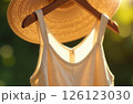 Summer casual dress and hat hanging on hanger in sunshine on green background, close-up 126123030