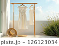 White women's clothes hang on a hanger on the terrace, a hat lies nearby, a clear sky in the background 126123034