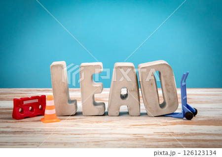 Lead Concept. Concrete alphabet letters on a light painted wood texture background 126123134