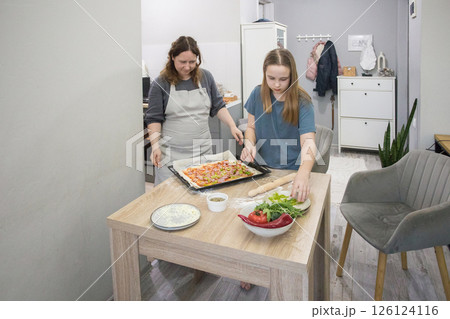 Young child girl with woman cooking homemade pizza in domestic kitchen together. Mother and daughter Young child girl with woman cooking homemade pizza in domestic kitchen together. Mother and daughter 126124116