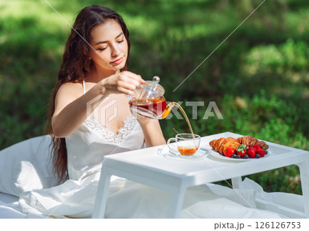 Young woman has breakfast in bed in a summer forest Young woman has breakfast in bed in a summer forest 126126753