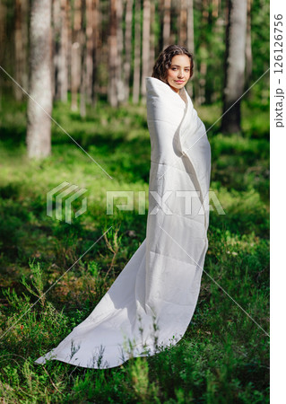 Woman stands in the woods wrapped in a blanket 126126756