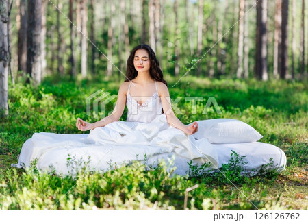 Young woman is sitting in the forest on a white bed Young woman is sitting in the forest on a white bed 126126762