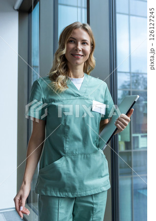 Pretty blonde female doctor in green lab coat near the window in the hospital Pretty blonde female doctor in green lab coat near the window in the hospital 126127245