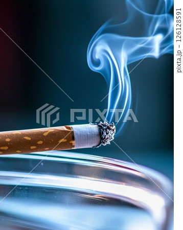 Lit cigarette with smoke curling upwards against a dark background represents smoking, addiction, and health risks 126128591