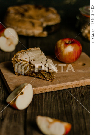 Traditional apple pie Charlotte. Sliced apples lie nearby. Sweet Thanksgiving dinner, autumn seasonal apple pie slice one piece on wooden tray, on dark wooden background Traditional apple pie Charlotte. Sliced apples lie nearby. Sweet Thanksgiving dinner, autumn seasonal apple pie slice one piece on wooden tray, on dark wooden background 126130408