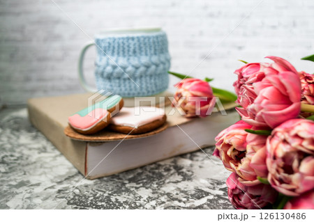 Pink tulips blurred foreground, open book and a mug of freshly brewed coffee or tea. Spring set. Pink tulips blurred foreground, open book and a mug of freshly brewed coffee or tea. Spring set. 126130486