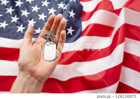 Woman hand holds military dogtag against backdrop of American flag. National pride and military tribute with focus on tag. Memorial Day. 126130875