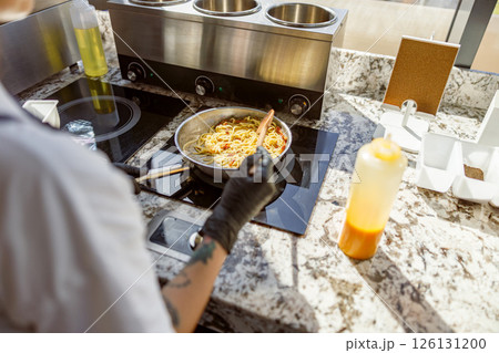 A skilled chef is cooking pasta in a modern kitchen with a stylish granite countertop A skilled chef is cooking pasta in a modern kitchen with a stylish granite countertop 126131200