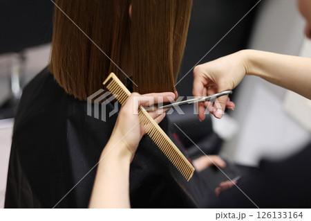 Unrecognisable hairdresser cutting female client hair with professional barber scissors and comb and making stylish haircut short bob hairstyle in beauty salon. Hair care, hair salon and hairstyling 126133164
