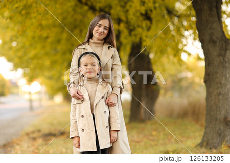 Family day, mother's day. Happy smiling young mom soft huggs her adorable child daughter, spend time together at autumn park, look at camera. Family look. Having fun outdoors on fall holiday 126133205