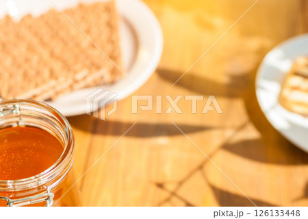 Orange Honey Jar on a Wooden Table With Wafers, Warm Sunlight Casting Shadows perfect for Cafes and Food Lovers Orange Honey Jar on a Wooden Table With Wafers, Warm Sunlight Casting Shadows perfect for Cafes and Food Lovers 126133448
