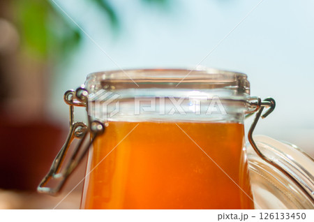 Golden Honey Jar Glistens in Sunlight on a Bright Countertop, Perfect for Health Shops, Food Blogs, and Organic Markets Golden Honey Jar Glistens in Sunlight on a Bright Countertop, Perfect for Health Shops, Food Blogs, and Organic Markets 126133450