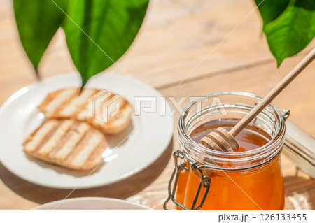 Honey Jar With Wooden Dipper Next to Toasted Bread in a Bright Kitchen, Highlighting Cafes, Bakeries, and Healthy Foods 126133455