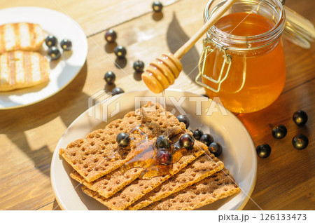 Honey Drizzled on Crackers With Berries on a Sunlit Wooden Table; Perfect for Food Bloggers and Gourmet Snack Lovers 126133473