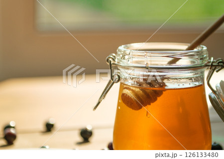 Honey Drips From a Wooden Dipper Into a Glass Jar, Softly Lit ideal for Food Blogs and Wellness Brands 126133480