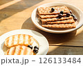 Breakfast Spread of Grilled Bread and Crisp Crackers on a Wooden Table, Bathed in Warm Sunlight perfect for Cafes and Food Blogs 126133484
