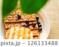 Whole Grain Crackers With Syrup and Blueberries on a Light Table, Highlighting Warmth and Texture for Food Blogs and Recipes 126133488