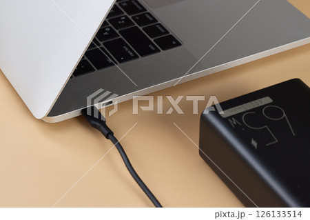 Charging laptop with power bank on beige background, close-up. Charging laptop with power bank on beige background, close-up. 126133514