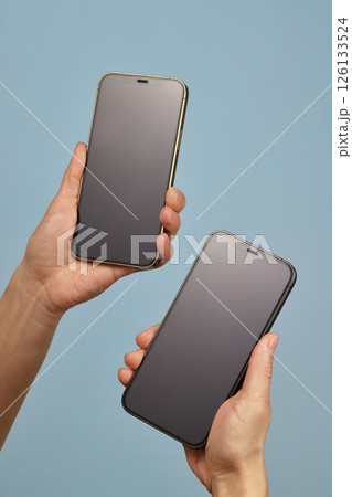 woman holding two smartphones with blank screens on blue background woman holding two smartphones with blank screens on blue background 126133524