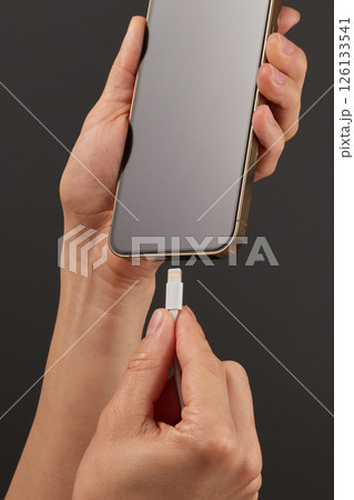female hand plugging charger cord into smartphone to charge battery on black background, Wired charging female hand plugging charger cord into smartphone to charge battery on black background, Wired charging 126133541