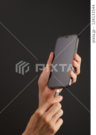 female hand plugging charger cord into smartphone to charge battery on black background, Wired charging 126133544