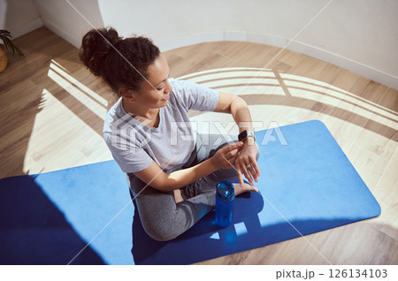 Woman Using Fitness Tracker While Relaxing on Yoga Mat in Bright Room 126134103