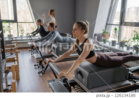 Womens doing Swan exercise on Pilates Reformer for the chest and back muscles, focusing on flexibility, strength, and control with determination 126134180