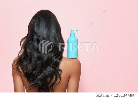 A woman showcasing her lustrous, wavy hair demonstrates a haircare product's versatility. The blue shampoo bottle on her shoulder emphasizes beauty, radiance, and healthy hair. Self-care and grooming. 126134494