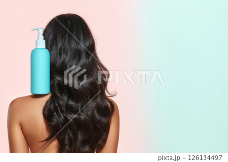 A woman showcasing her lustrous, wavy hair demonstrates a haircare product's versatility. The blue shampoo bottle on her shoulder emphasizes beauty, radiance, and healthy hair. Self-care and grooming. 126134497