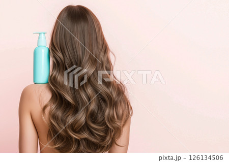 A woman showcasing her lustrous, wavy hair demonstrates a haircare product's versatility. The blue shampoo bottle on her shoulder emphasizes beauty, radiance, and healthy hair. Self-care and grooming. 126134506