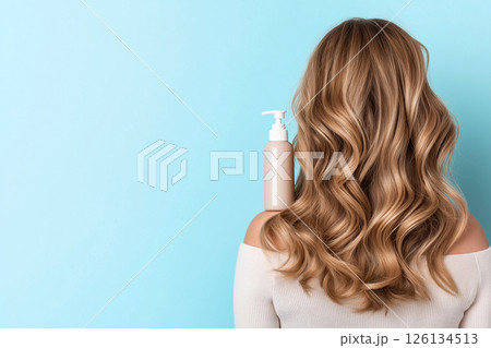 A woman showcasing her lustrous, wavy hair demonstrates a haircare product's versatility. The blue shampoo bottle on her shoulder emphasizes beauty, radiance, and healthy hair. Self-care and grooming. 126134513