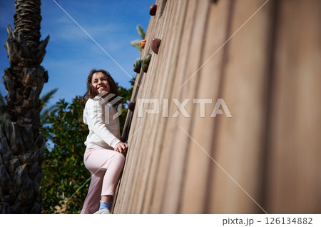 Smiling Young Girl Climbing an Outdoor Wall on Sunny Day Smiling Young Girl Climbing an Outdoor Wall on Sunny Day 126134882