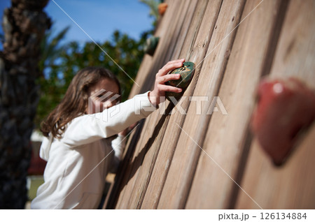 Young Girl Engaging in Outdoor Climbing Activity on a Wooden Wall Young Girl Engaging in Outdoor Climbing Activity on a Wooden Wall 126134884