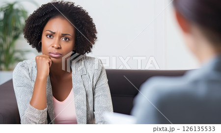 Middle aged dark-skinned woman at an appointment with a psychologist. She delves into the problem and helps the patient solve the problem. The psychotherapist listens carefully to the patient’s story. 126135533