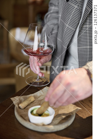 Champagne tasting in restaurant, A man holds in his hand a beautiful elegant glass with rose sparkling wine, He eats delicious snacks and drinks pink wine Champagne tasting in restaurant, A man holds in his hand a beautiful elegant glass with rose sparkling wine, He eats delicious snacks and drinks pink wine 126137371