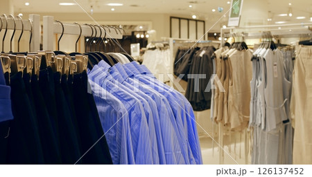 Fashion retail store interior featuring neatly hanging blue shirts and dark trousers alongside various garments, showcasing clothing display and retail merchandise arrangement. Concept fashion clothes 126137452