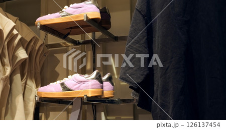 Trendy purple sneakers with brown soles positioned on sleek metal rack alongside black and light colored t shirts within contemporary retail clothing environment. Concept fashion clothes 126137454