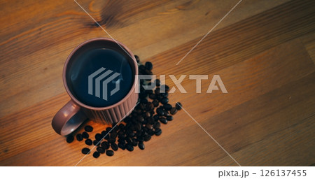 Roasted beans encircle hot cup on rustic wood, aroma drifting upward creating ambiance, coffee aroma artisan craft, aroma enticing viewers, asset for brands and sensory marketing visuals. 126137455